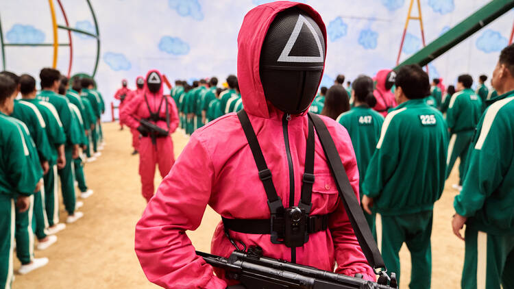 A scene from the Netflix Show 'Squid Game' of a masked guard in a pink jumpsuit.