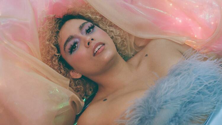 The singer Kee'ahn dressed in a blue top and laying on pink tulle.