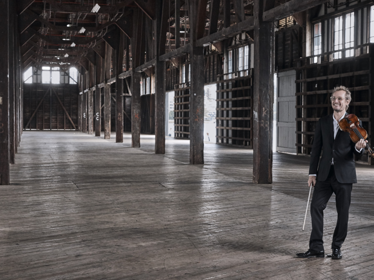 Richard Tognetti stnads inside the ACO's new venue at Pier 2/3 holding a violin 