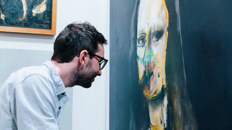 A man wearing glasses looks up close at a portrait