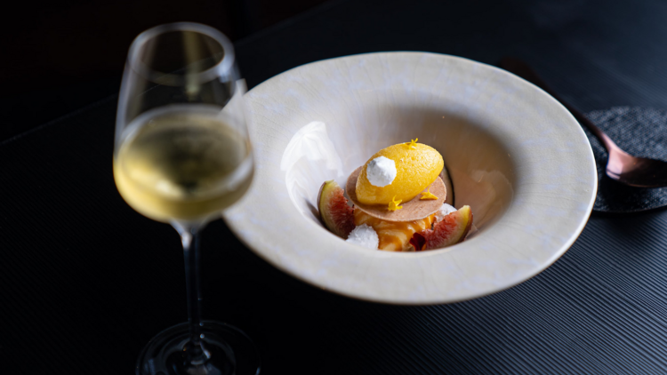 In a deep white dish is a dessert of lemon sorbet, a glass of white wine in the foreground