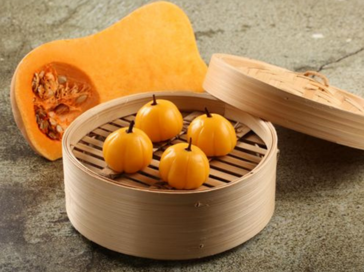 A dumpling steamer with four pumpkin shaped dumplings in the centre