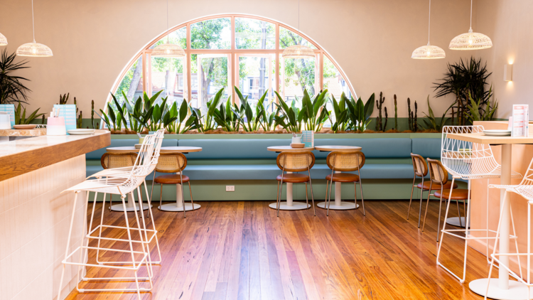 A bar and tables with pink walls, warm wooden floors and blue leather banquette seating