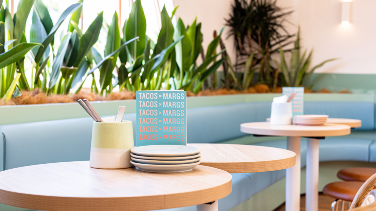 A bar and tables with pink walls, warm wooden floors and blue leather banquette seating