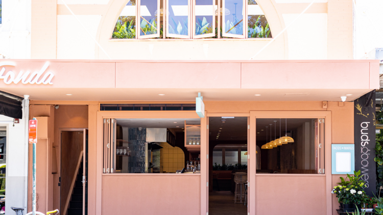 Exterior shot of restaurant from across street. Pastel pink walls with the word Fonda on left 