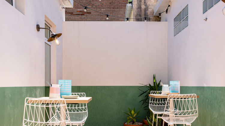 Courtyard with white tables, white walls with a green stripe and festoon lighting