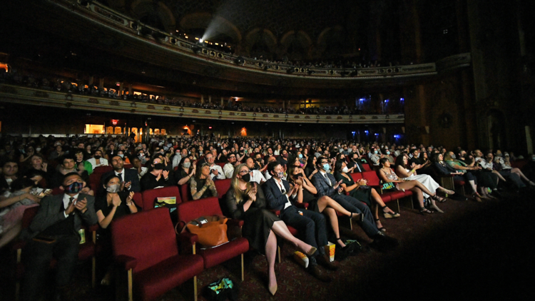 An audience wearing facemasks is gathered to watch a film in the darkened State Theatre