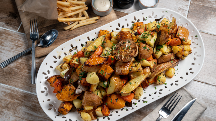 A white oval plate of roasted vegetables, a packet of chips in the background