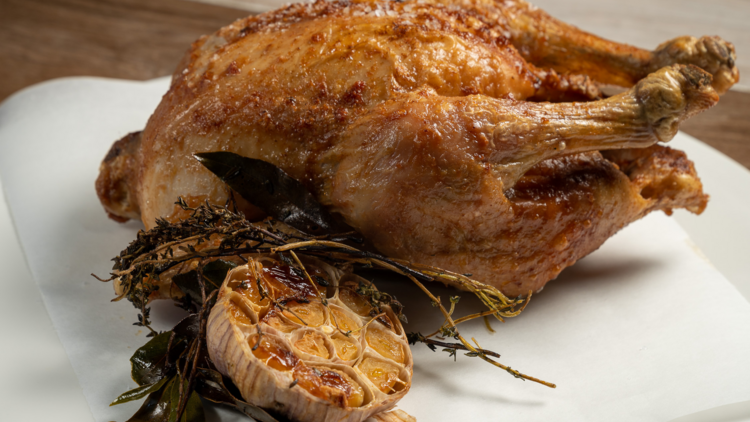 A roasted chicken with a half head of garlic and bay leaves