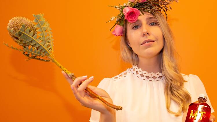 A promotional image for WellBless, in which writer and actress Ella Roth Barton  wears a flowy white dress and holding a mysterious bottle of something and a dried flower