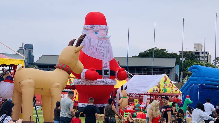 Families at the Sydney Christmas Fair with large a santa and reindeer figure in the background