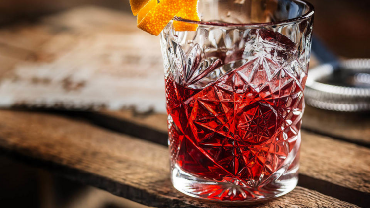 On a rustic wooden crate is a negroni garnished with a twist of orange peel