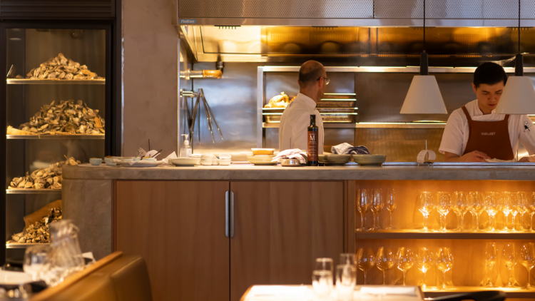 The open kitchen, wine glasses stacked in a cupboard in front and piles of oysters in their shells in a fridge to the left.