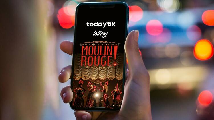 A hand holding up a smartphone with TodayTix's Moulin Rouge lottery on the screen