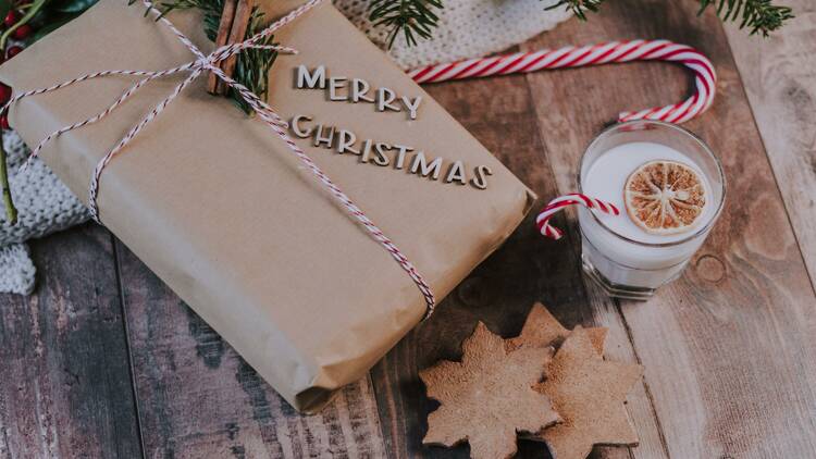 A brown paper wrapped present next to a candy cane and a glass of milk.