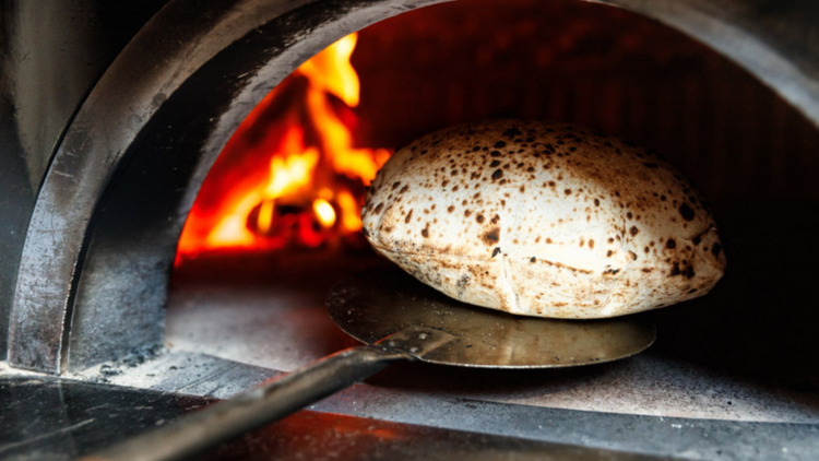 Woodfired bread it puffed up and charred on top of a paddle