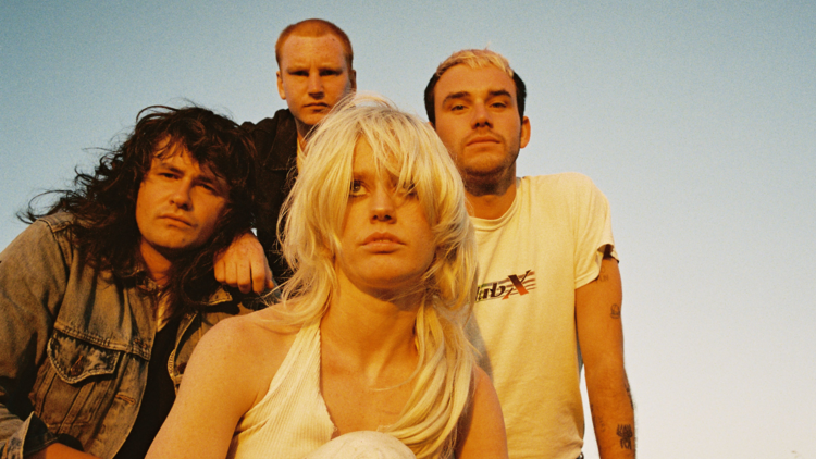 The band Amyl and the Sniffers crouch in front of a dusty sky