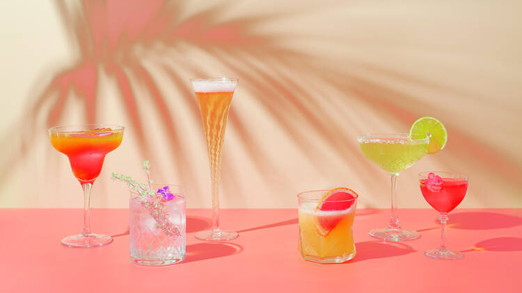 A line-up of six different cocktails – all in different glasses – against a pink backdrop