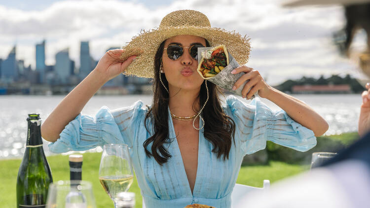 A woman holding a Gyro blows a kiss to the camera, with Sydney Harbour in the background