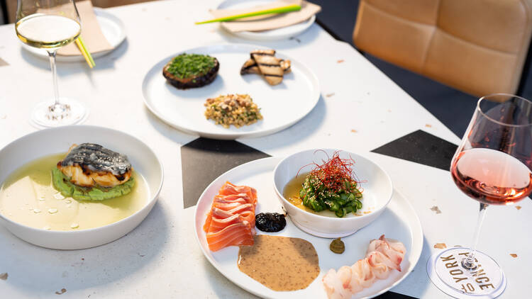 A table loaded with bright white plates with pops of colourful food: bright raw salmon, seared fish, green peas and more. 