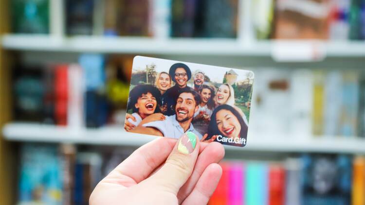 A person holds up a gift card with a photo of a group of people printed on it