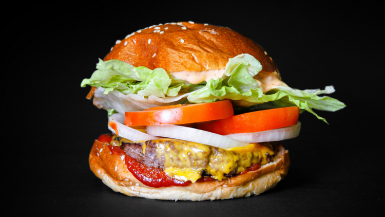 On a black background, an American style buger with tomatoes, onions, lettuc, cheese and a vegan meat patty