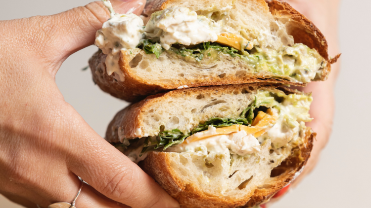 A pair of hands holding two halves of a pesto and poached chicken sandwich.