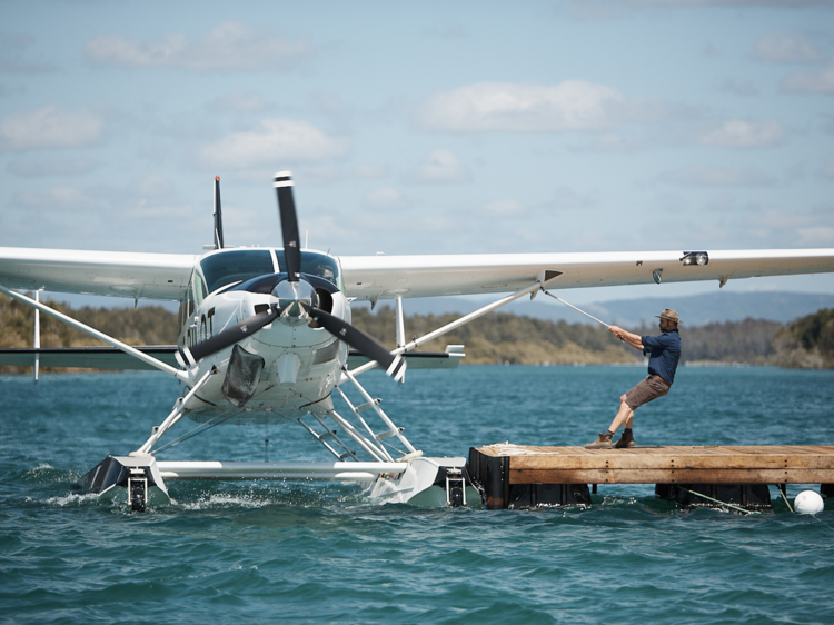 A seaplane is being pulled by hand towards a pontoon by an oyster farmer