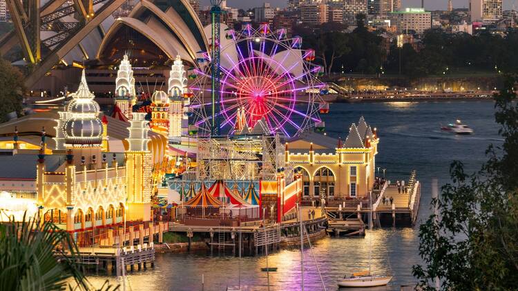 Luna Park buildings and ferris wheel covered in fairylights at dusk on the harbour.