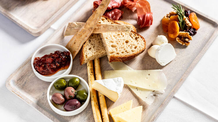 A photo of a cheese and meat board with olives, dried fruit, and crusty bread