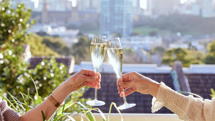 Photo of two people cheersing with champagne glasses to a cityscape view