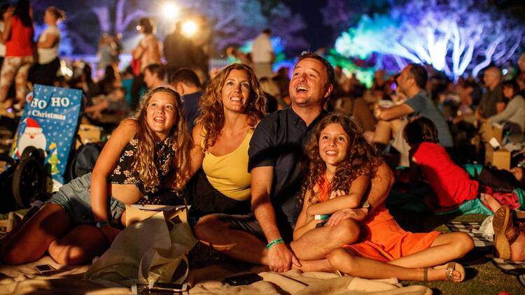 A photograph of a family sitting on a picnic rug watching fireworks