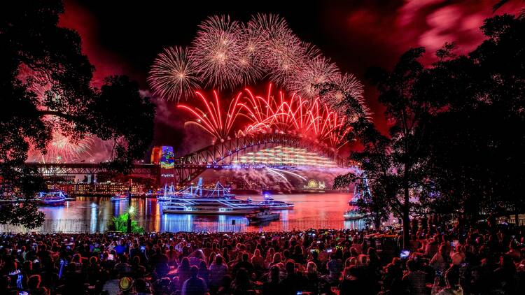 A large crowd of people sitting on the lawn watching the Sydney NYE fireworks