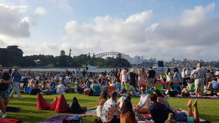 A large crowd of people having a picnic on the lawn with a view of the Sydney harbour bridge