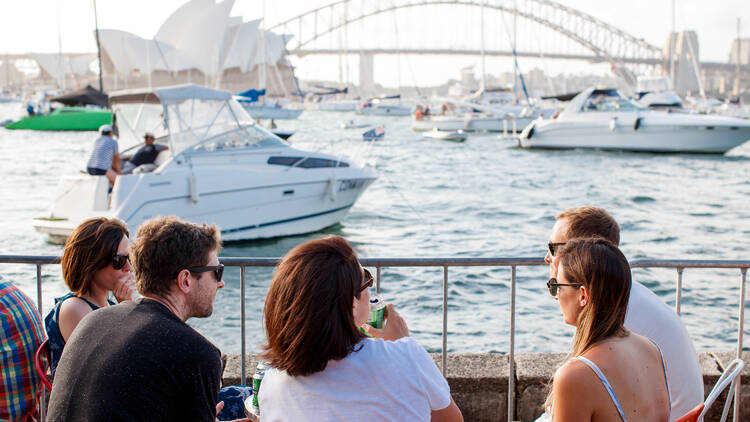 A photograph of a family sitting at a table with a view of severalboats, the Sydney harbour bridge and opera house