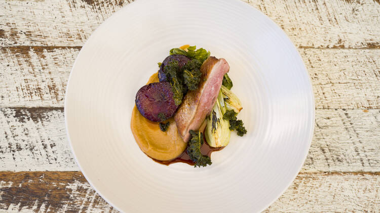 An aerial shot of a white plate with a carefully constructed dish of meat and vegetables