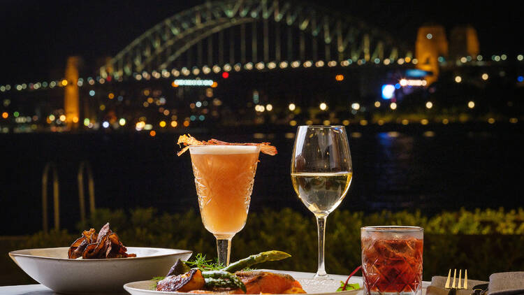 A table at the Fenwick, laden with drinks and plates of food, with the Harbour Bridge in the background