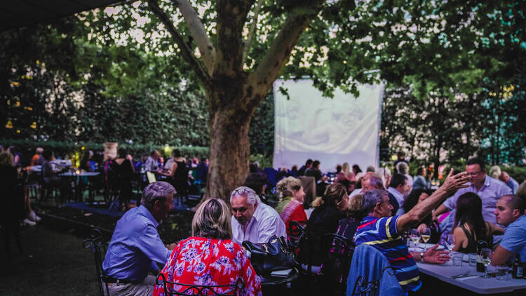 A busy courtyard filled with people sitting, eating and drinking. 
