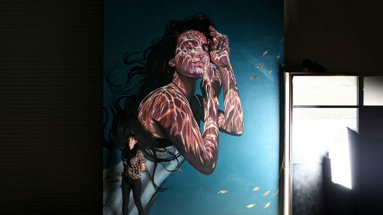 Loretta standing in front of a mural of a woman submerged in water.
