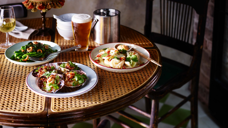 Plates of food and a beer on a wicker table