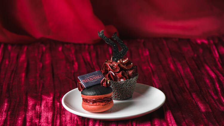A black and red macaron topped with a Moulin Rouge! chocolate and a cupcake with red icing. 