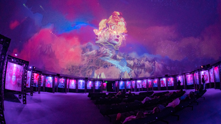 An audience seated under a dome cinema watches a psychedelic 360 degree movie