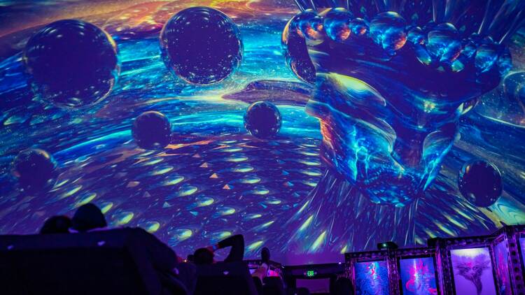 An audience seated under a dome cinema watches a psychedelic 360 degree movie