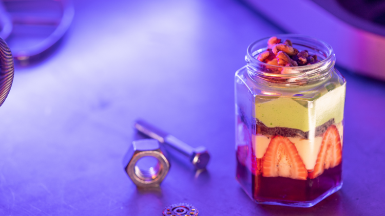 A jar of trifle on a purple background with little nuts and screws next to it