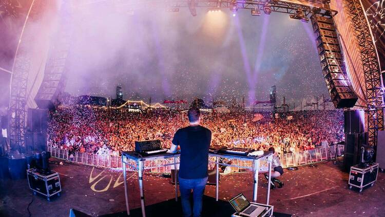 A DJ playing a set on a main stage facing out into a large crowd.