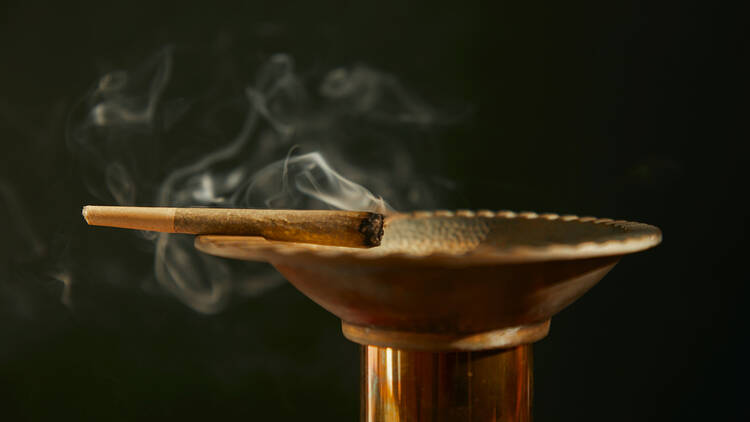 A gold ash tray with a smoking joint resting on the edge