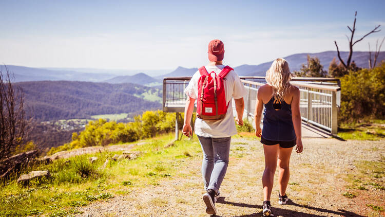 A man and a woman walk towards a viewing platform overlooking a lush valley