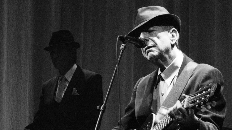 A black and white photo of singer Leonard Cohen performing with a guitar.