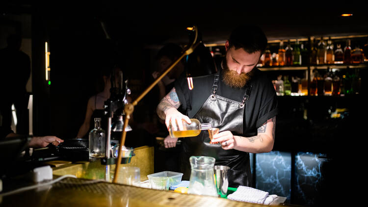 A bartender pouring a beverage into a shot glass in a dimly lit bar.