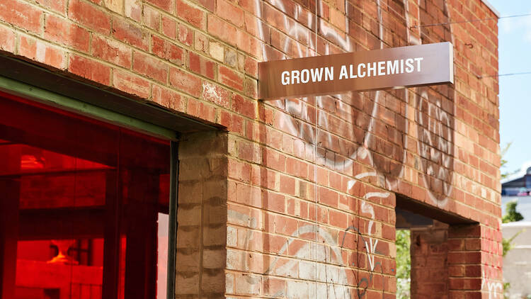 A brick building with red glass that has a sign reading Grown Alchemist. 